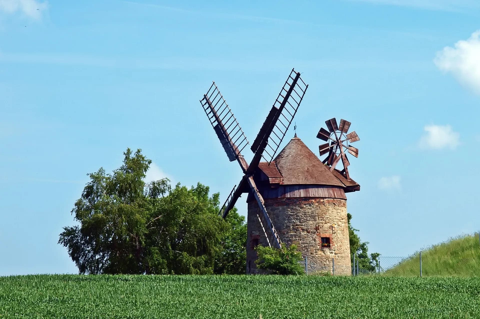 BookNoFees Beispielbild: Historische Windmühle mit Flügeln zwischen grünen Bäumen
