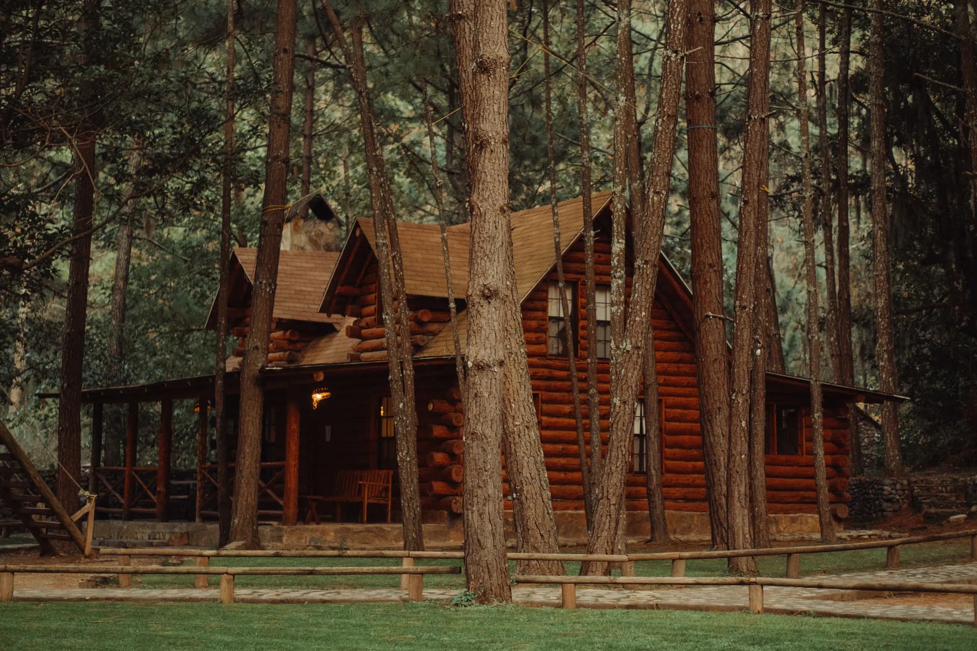 BookNoFees Beispielbild: Blockhütte mit überdachter Terrasse zwischen hohen Waldbäumen