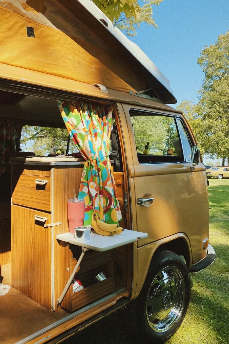 BookNoFees Beispielbild: Geöffneter gelber Campingbus mit Holzausbau und bunten Vorhängen im Sonnenschein