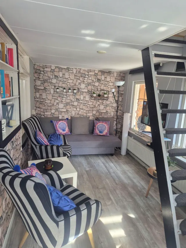 BookNoFees: Ferienwohnung in Domburg, Zeeland, Niederlande – Wohnzimmer mit Wand im Steinmuster, gestreiften Sesseln, einem grauen Sofa und einer Wendeltreppe