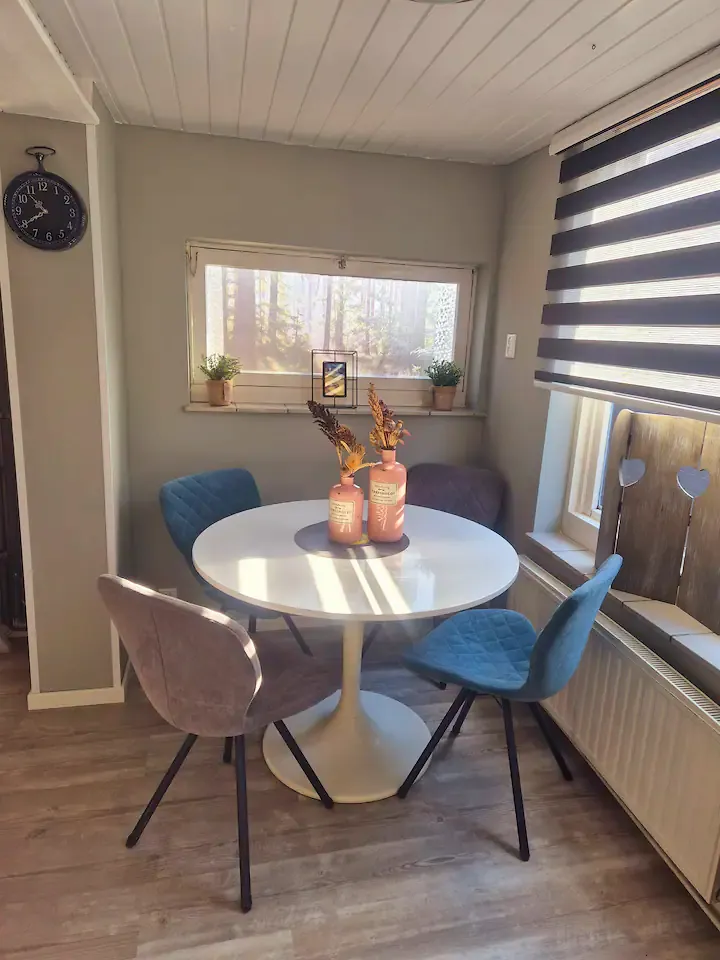 BookNoFees: Ferienwohnung in Domburg, Zeeland, Niederlande – Essbereich mit rundem weißem Tisch, blauen und grauen Stühlen und einem Fenster mit Blick auf den Wald