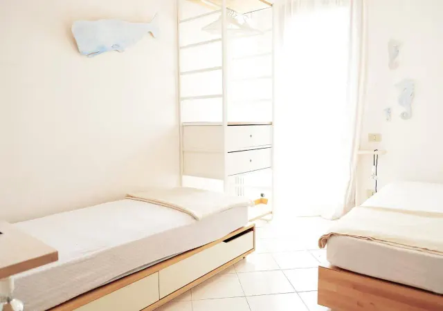 BookNoFees: Ferienwohnung in Cavallino-Treporti, Italien – Zwei Betten in einem Schlafzimmer mit weißen Wänden im „Sunny Apartment On The Sea“ in Cavallino-Treporti