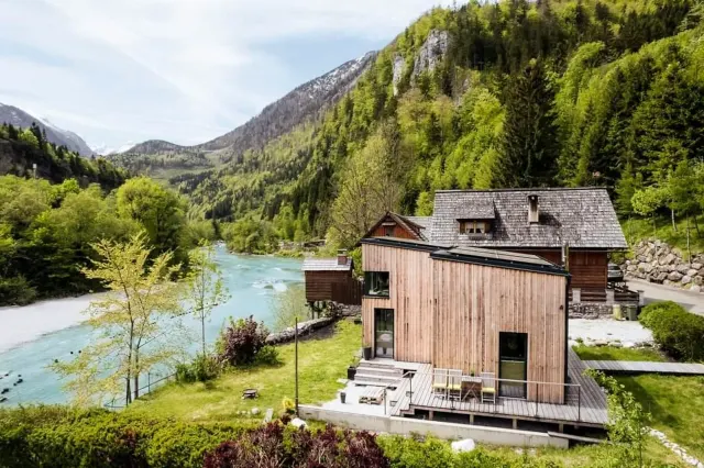 BookNoFees: Ferienwohnung in Hieflau – Außenansicht eines Ferienhauses aus Holz vor dem Hintergrund von Fluss und Bergen