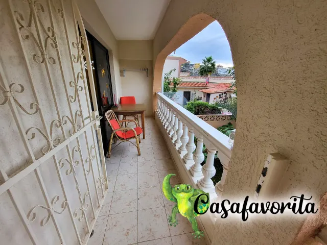 BookNoFees: Ferienwohnung in Buen Paso, Teneriffa, Spanien – Balkon mit Tisch, roten Stühlen und Blick auf die Dächer und Palmen