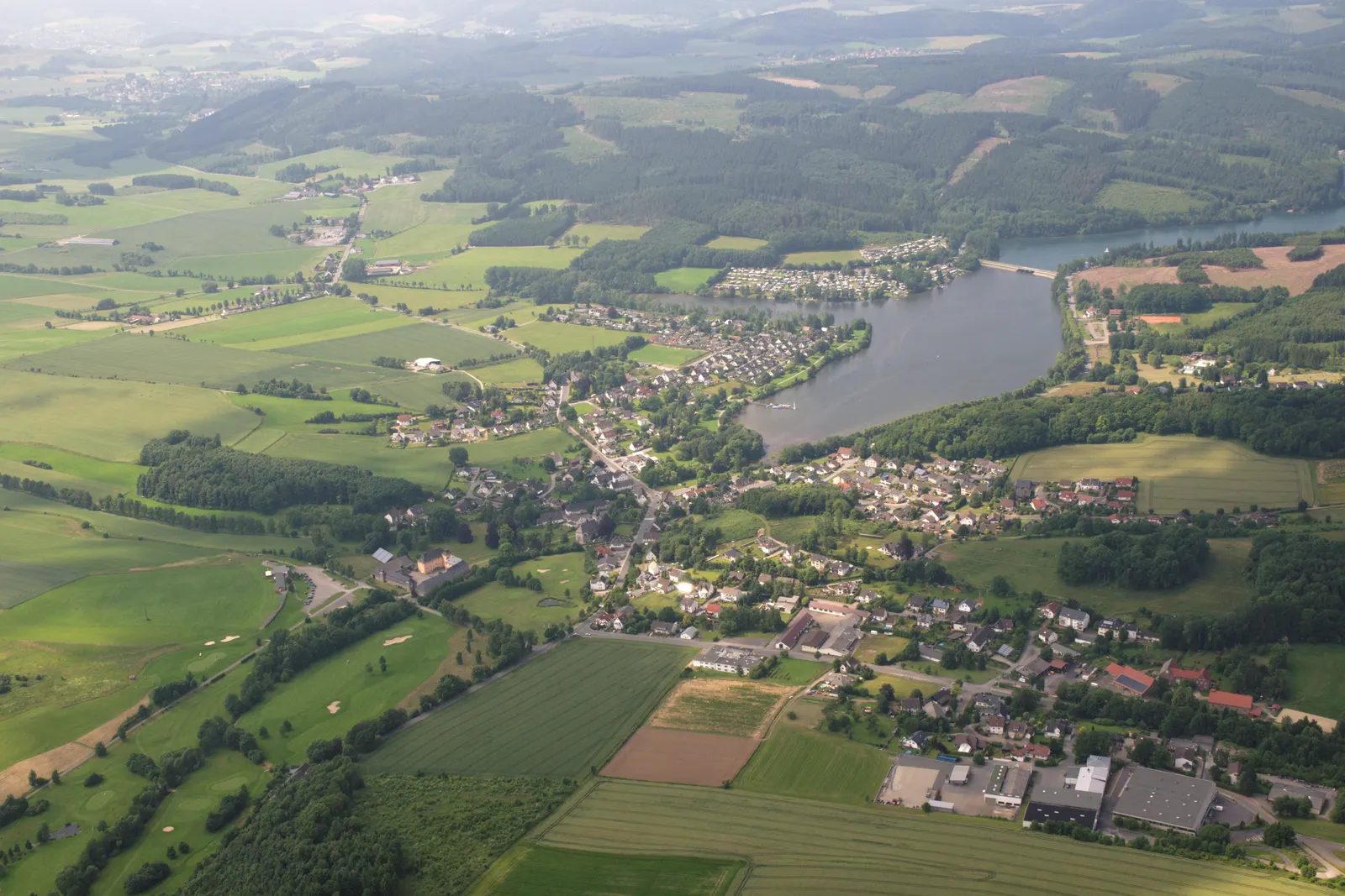 Der Sorpesee aus der Vogelperspektive, mit dem Dorf Amecke an seinem Ostufer und den bewaldeten Hügeln des Sauerlands im Hintergrund