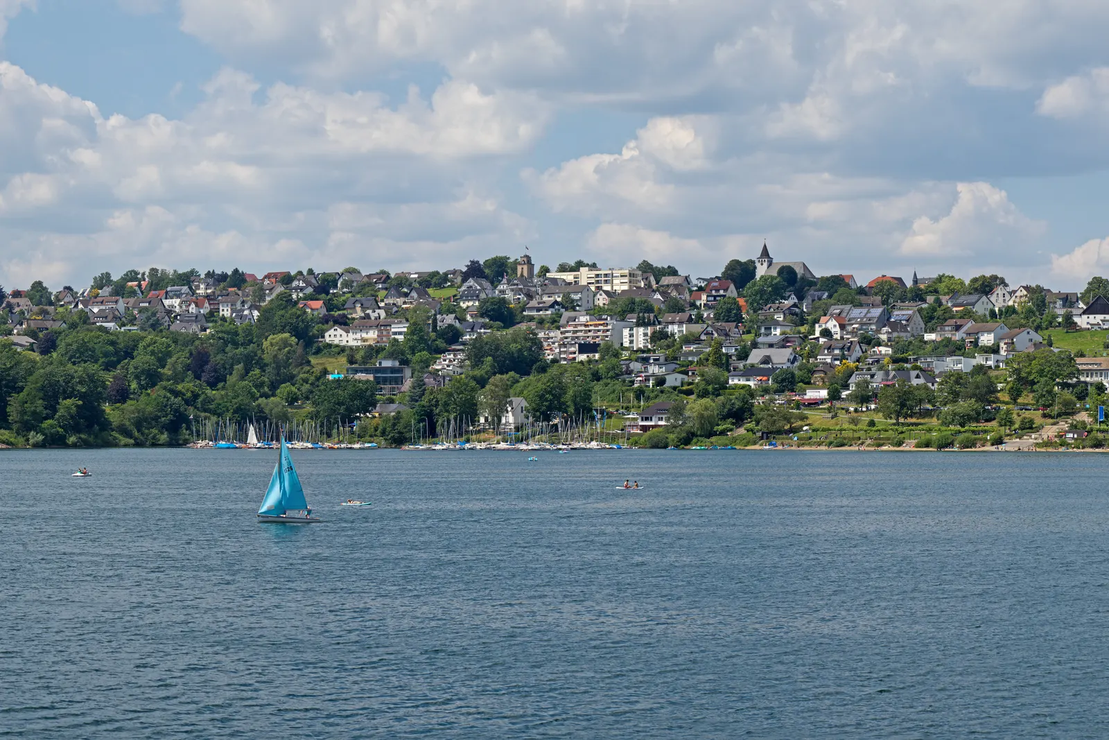 BookNoFees, Langscheid am Sorpesee bei Sundern: das Dorf am Seeufer hoch über dem Wasser, mit einem Segelboot im Vordergrund, Sundern (Sauerland), Deutschland