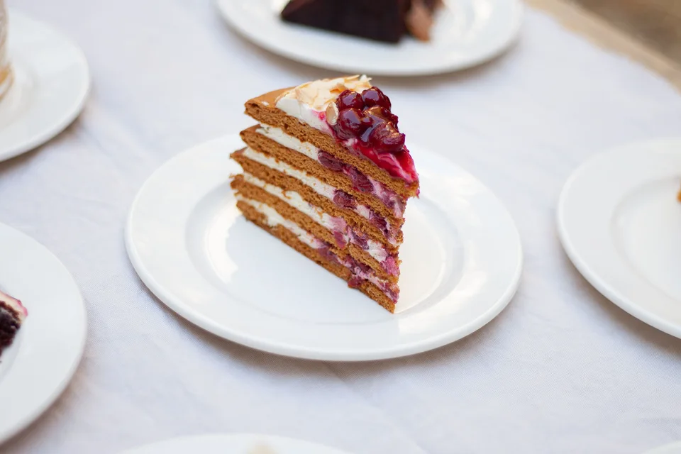 BookNoFees: Beispielfoto: Ein Stück Schichtkuchen mit Beeren als Garnitur auf einem weißen Teller