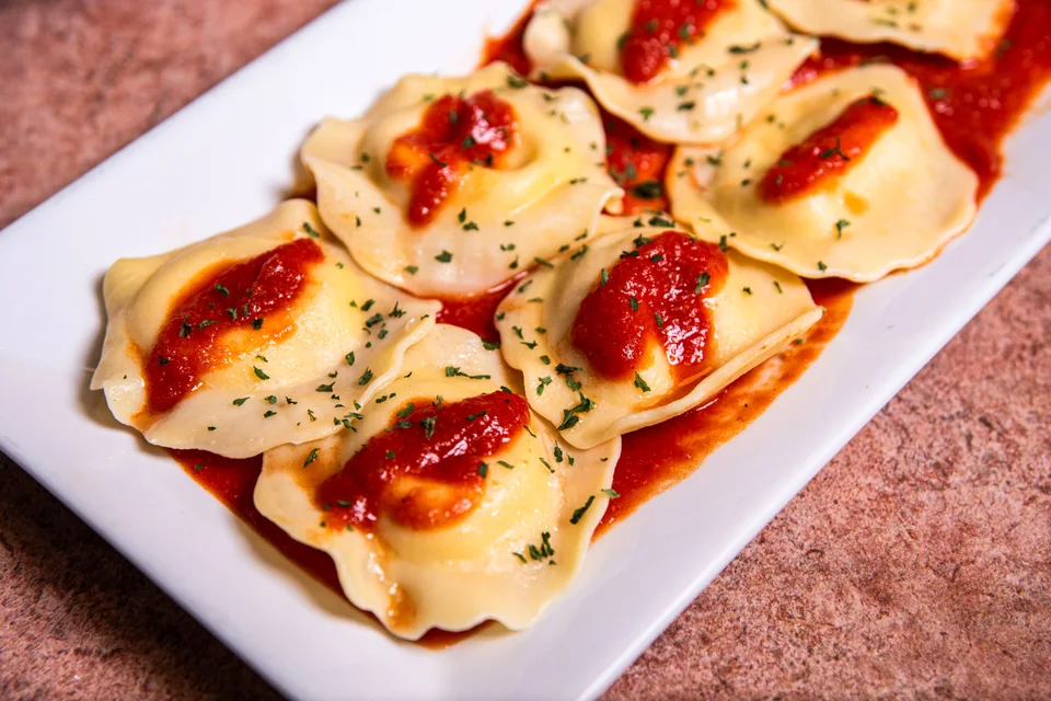 Beispielfoto: Ravioli mit Tomatensoße und Kräutern auf einem weißen Teller